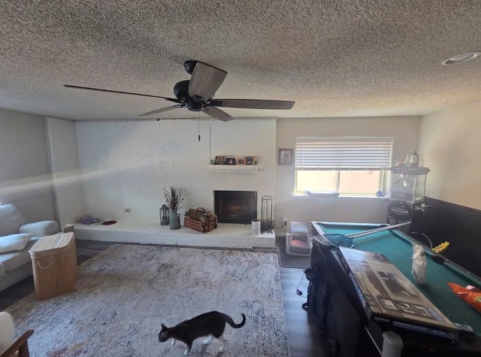 Living room before renovation with an all white painted brick fireplace and dated flooring